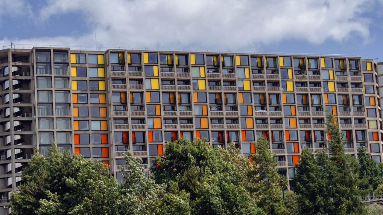 Tall modern apartment building with colorful yellow and orange window frames and trees in front