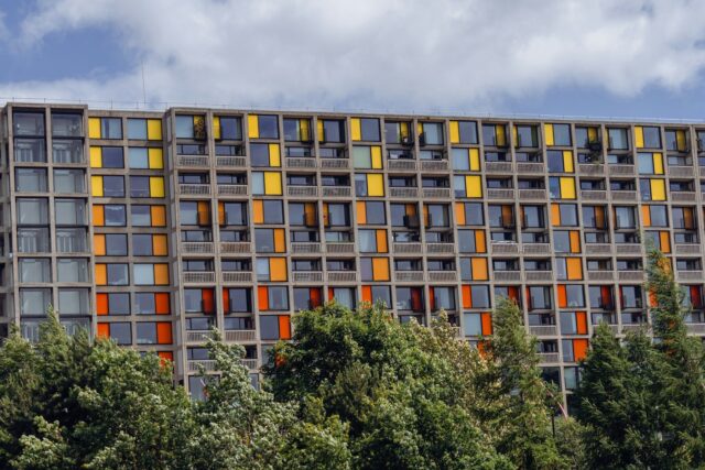 Tall modern apartment building with colorful yellow and orange window frames and trees in front