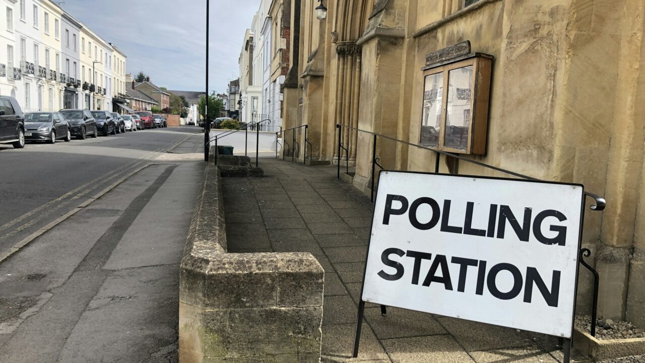 A polling station sign attached to a stone building on a British high street.