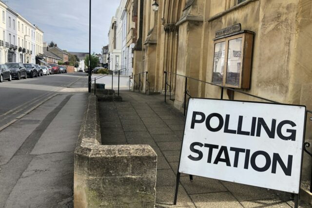 A polling station sign attached to a stone building on a British high street.